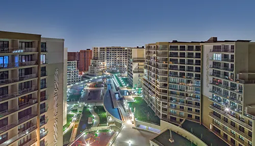 Evora İstanbul konut sitesi akşam saatinde: iki yanda ışıkları yanan bloklar, ortada aydınlatılmış avlu ve yürüyüş yolu