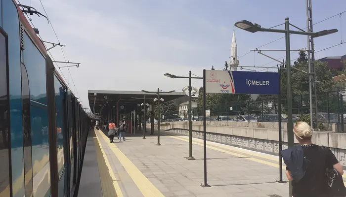 İçmeler Marmaray İstasyonu peronu: solda perona yanaşmış tren, sağda mavi İÇMELER tabelası, arkada cami minaresi