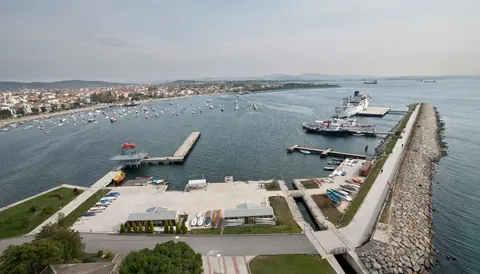 Havadan Tuzla koyu: solda demirli tekneler ve iskele, ortada rıhtıma yanaşmış gemi, sağda dalgakıran