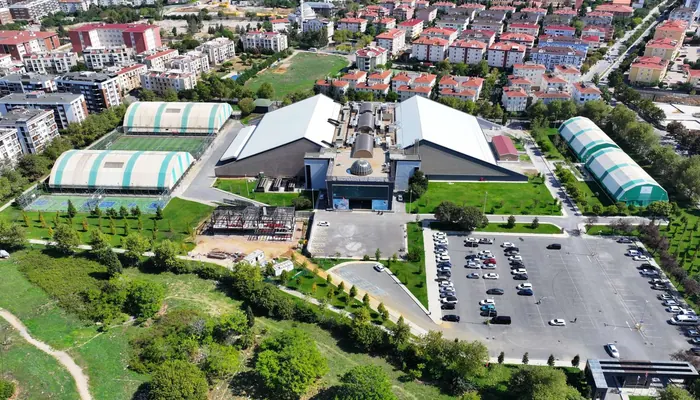 Spor kompleksinin havadan görünümü: ortada kapalı salon, iki yanında yeşil çizgili balon sahalar, sağ altta otopark