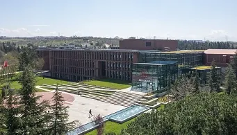 Koç Özel Lisesi yerleşkesi: kırmızı tuğla ana bina, önünde camlı giriş bölümü ve basamaklı meydan