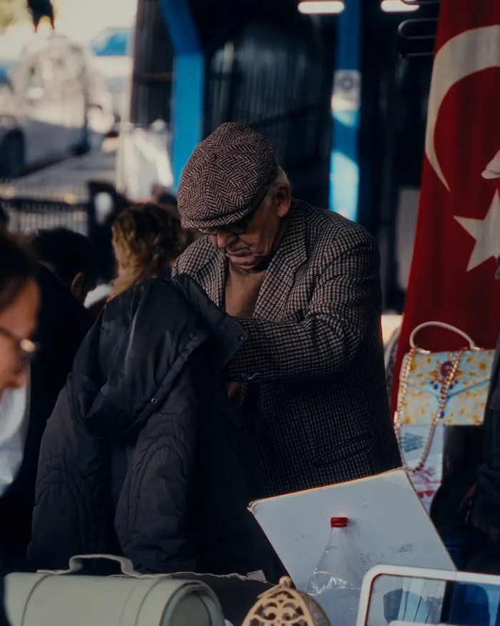 Tuzla Bit Pazarı — ikinci el eşya pazarında bir tezgâh: satıcı elindeki montu inceliyor, tezgâhta çanta, fener ve bavul (temsili görsel)