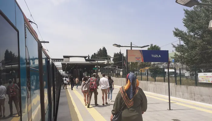Tuzla Marmaray İstasyonu peronu: solda perona yanaşmış tren, peronda yürüyen yolcular, sağda mavi TUZLA tabelası