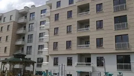 TOKİ konut bloğu: balkonlu cephe, önünde açık hava spor aletleri ve ahşap kameriye