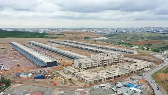 İnşaat hâlindeki hal tesisinin havadan görünümü: iki uzun hangar, ortada kaba inşaatı süren idari bina, çevresi şantiye