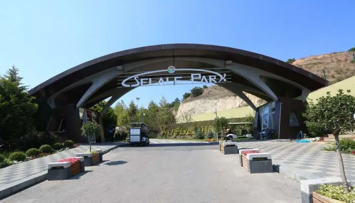 Şelale Park'ın giriş kemeri: üzerinde park adı yazılı, altından geçen yol, sağda tepe yamacı
